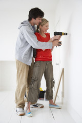 Side view of a young man and woman drilling hole in the wall at their new home