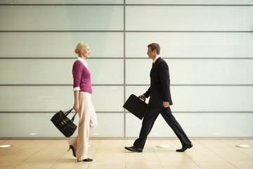 Profile shot of businesspeople with handbags walking in office corridor - Powered by Adobe