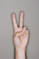 Closeup of a man's hand gesturing peace sign against gray background