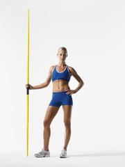 Full length portrait of a young female athlete holding javelin against white background