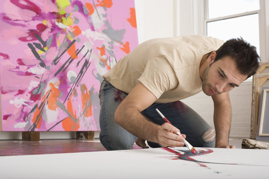 Young man painting on canvas on studio floor