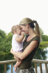 Fototapeta premium Happy young mother carrying daughter on balcony against the lake
