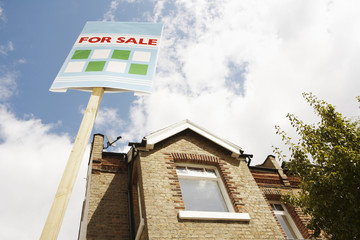 Low angle view of sale sign in front of new house against cloudy sky