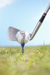 Golf ball with hundred dollar logo on tee with driver ready to tee off