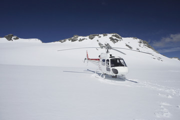 Helicopter landing on snowy mountain top against blue sky