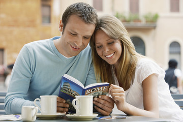 Smiling young couple at outdoor cafe looking at guidebook of Rome