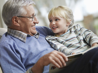 Happy little girl with grandfather reading story book at home