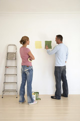 Full length rear view of a woman watch man testing paint colors on wall