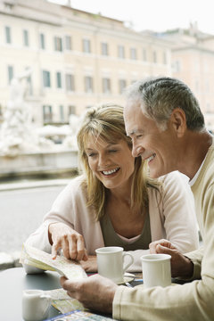 Happy Middle Aged Couple At Outdoor Cafe Reading Map In Rome