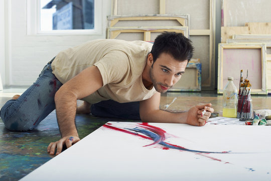 Young male artist looking at canvas on studio floor