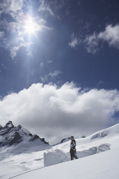 Side view of a mountain climber standing on snowy slope against clouds and sun