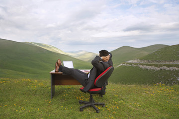 Naklejka premium Side view of businessman relaxing with feet on desk in mountain field