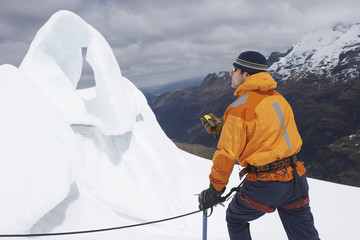 Mountain climber holding compass near ice formation in snowy mountains
