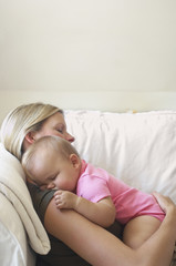 Side view of a young mother with baby sleeping on sofa at home