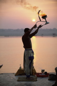 Hindu man worshipping in front of setting sun, River Ganges (Ganga), Varanasi (Benares), Uttar Pradesh state