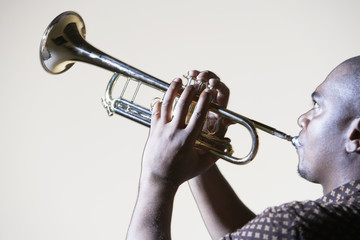 Side view of an African American man playing trumpet against gray background