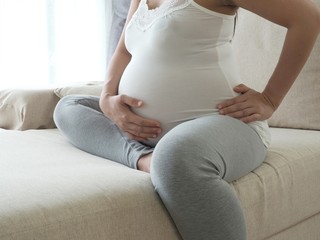 Pregnant woman with painful back in living room. Concept of pregnancy healthcare.