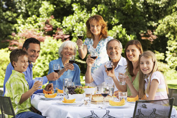 Portrait of happy family holding wine glasses at table in back yard