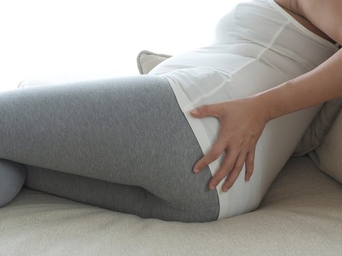 Pregnant woman with painful back on the sofa. Concept of pregnancy healthcare.