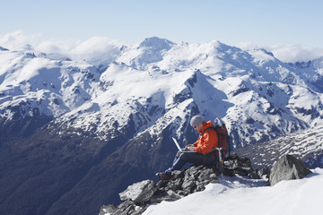Side view of a male mountain climber using laptop on mountain peak