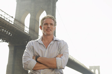 Smiling man standing with arms crossed against Brooklyn bridge