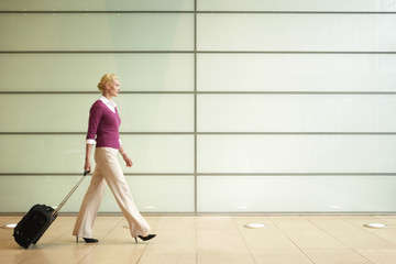 Side view of young businesswoman with suitcase walking in passage of office