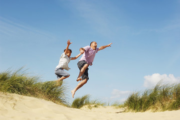 Cheerful father and son holding hands and jumping on sand at beach