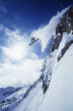 Low angle view of skier jumping from mountain against cloudy sky