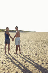Full length rear view portrait of a couple standing hand in hand at beach