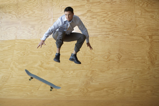 Full length of confident businessman with skateboard jumping against wood paneling