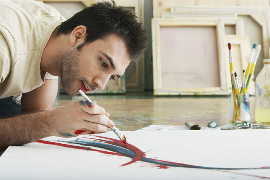 Closeup of a young man painting on canvas on studio floor