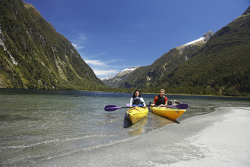 Two young people kayaking in the lake with mountains in background