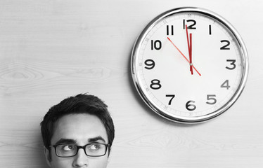 Headshot young businessman wearing spectacles looking at clock on wall in office - Powered by Adobe