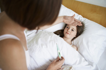 Mother checking temperature of daughter with thermometer in bed