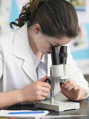 Teenage girl looking through microscope in laboratory