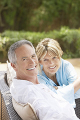 Portrait of smiling middle aged couple sitting on outdoor chairs