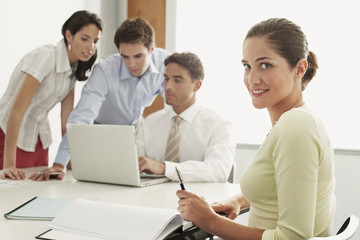 Portrait of beautiful young businesswoman sitting with colleagues working on laptop at desk in office