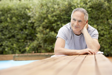 Happy middle aged man reclining by poolside