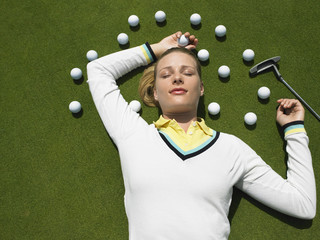 Beautiful female golfer lying on putting green with golf balls and club