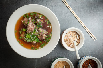Asian style pork bone soup with seasoning on dark stone background