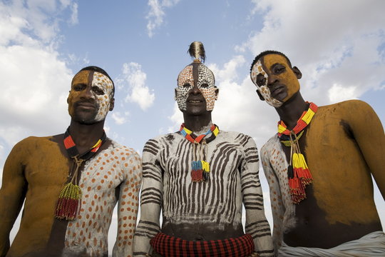 Three Karo tribesmen with face and body decoration in chalk, imitating the spotted plumage of the guinea fowl, Omo river, Lower Omo Valley, Ethiopia
