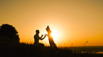Fototapeta na wymiar Couple - Man Getting Down on his Knee and Proposing to Woman high hill - Gets Engaged at Sunset - Putting Ring Girl's Finger