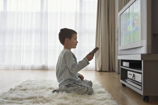Side view of a boy sitting on floor and watching cartoons in television
