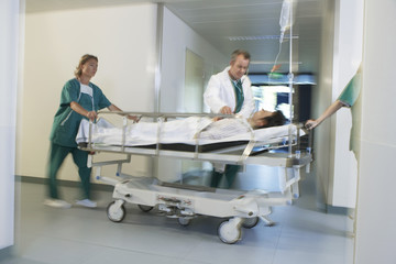 Medical workers moving patient on gurney through hospital corridor - obrazy, fototapety, plakaty