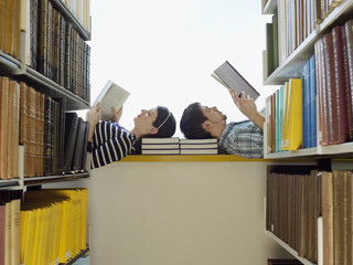 Male and female students lying on windowsill and reading in library 