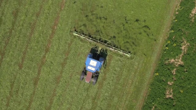 AERIAL: Flying above tractor tedding mowed hay with rakes on farmland field