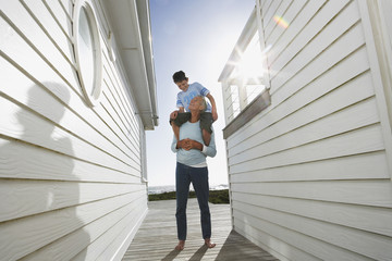 Full length of grandfather carrying grandson on shoulders between beach houses