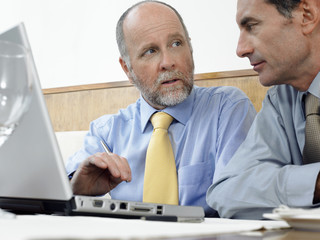 Obraz premium Middle aged businessman with colleague using laptop in restaurant