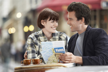 Happy young couple with a guidebook at an outdoor cafe