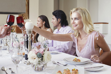 Beautiful young woman toasting red wine with friends at dinner table